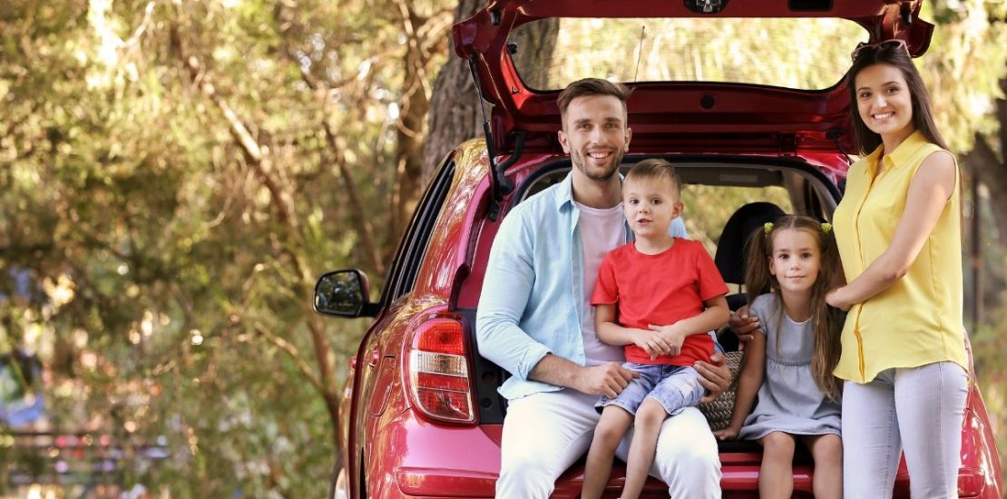 a family is sitting in the trunk of a red car